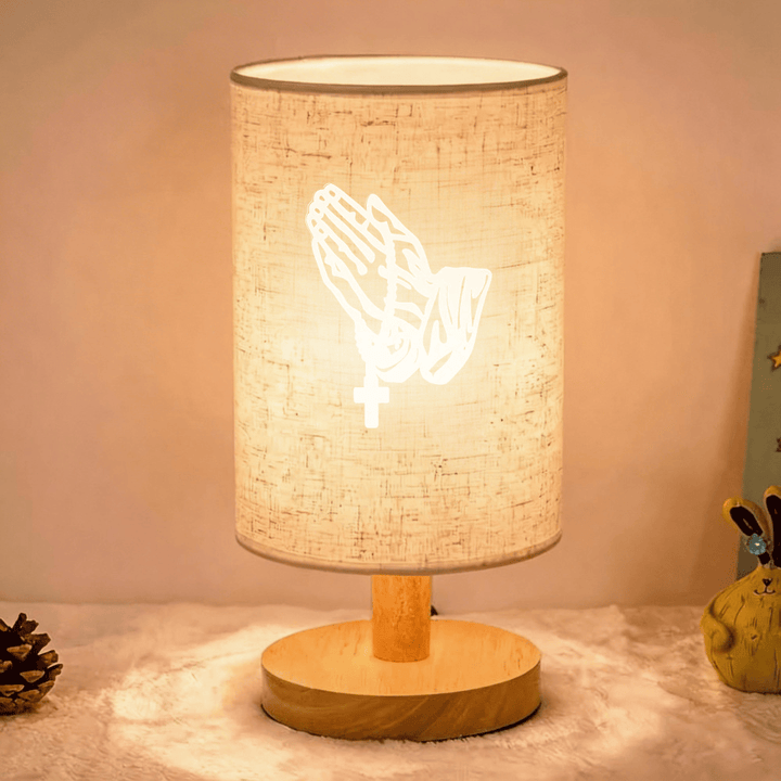 Christianartworkshop Lampada da tavolo con base in legno naturale e paralume in tessuto, motivo mani in preghiera con croce: un'oasi di pace e devozione notturna. - Attraverso - image 0